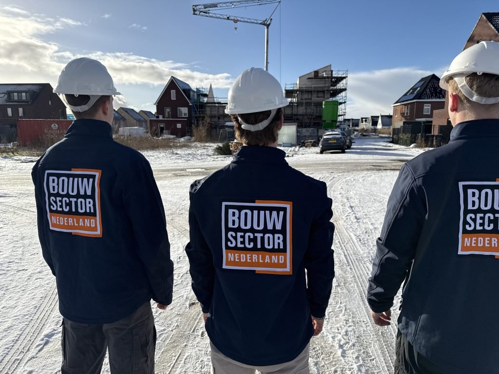 Drie vakmensen van Bouwsector Nederland met witte helm en jas met logo op een bouwplaats